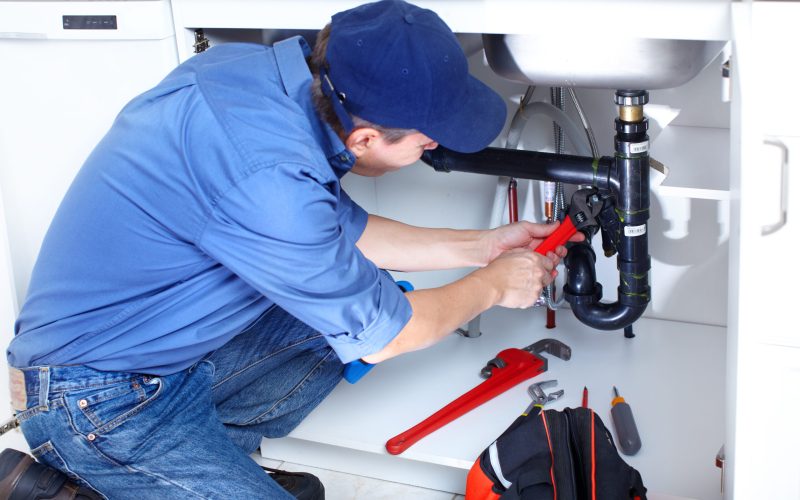 Mature plumber fixing a sink at kitchen